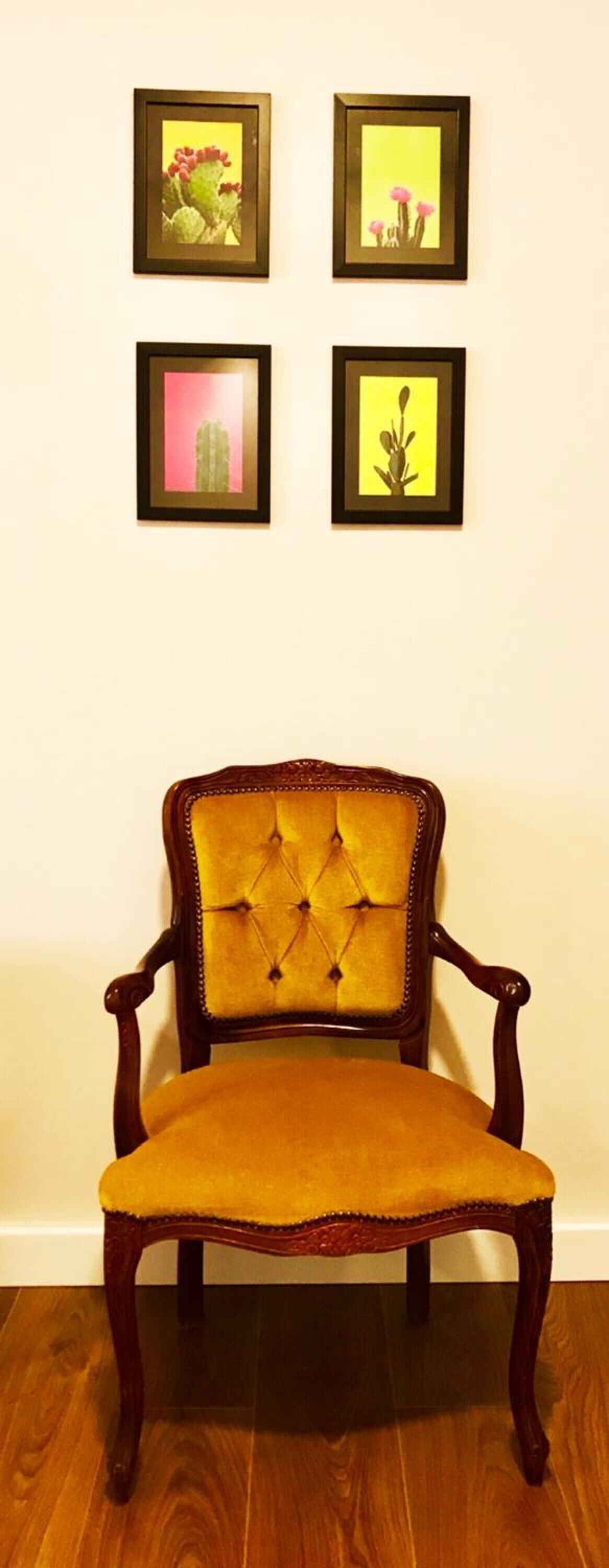 Une chaise dotée d’un dossier capitonné et d’un siège jaune, placée devant un mur orné de quatre tableaux encadrés.