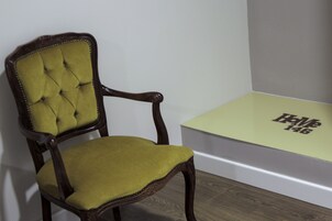 Una silla de madera con respaldo capitonado y asiento acolchado, ubicada junto a una mesa verde claro con un logotipo.