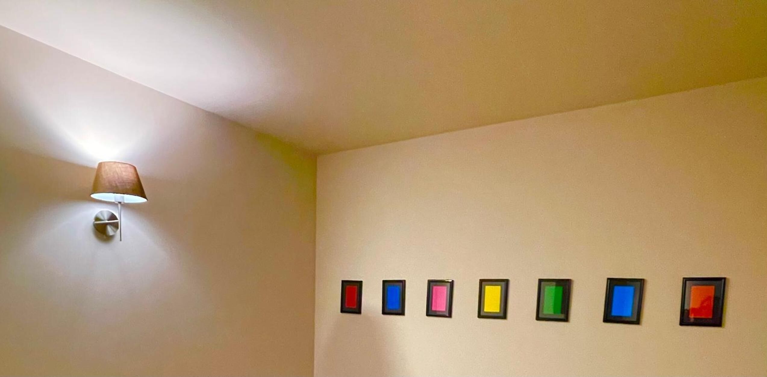 Una habitación con una lámpara fijada a la pared y una hilera de cuadros enmarcados.