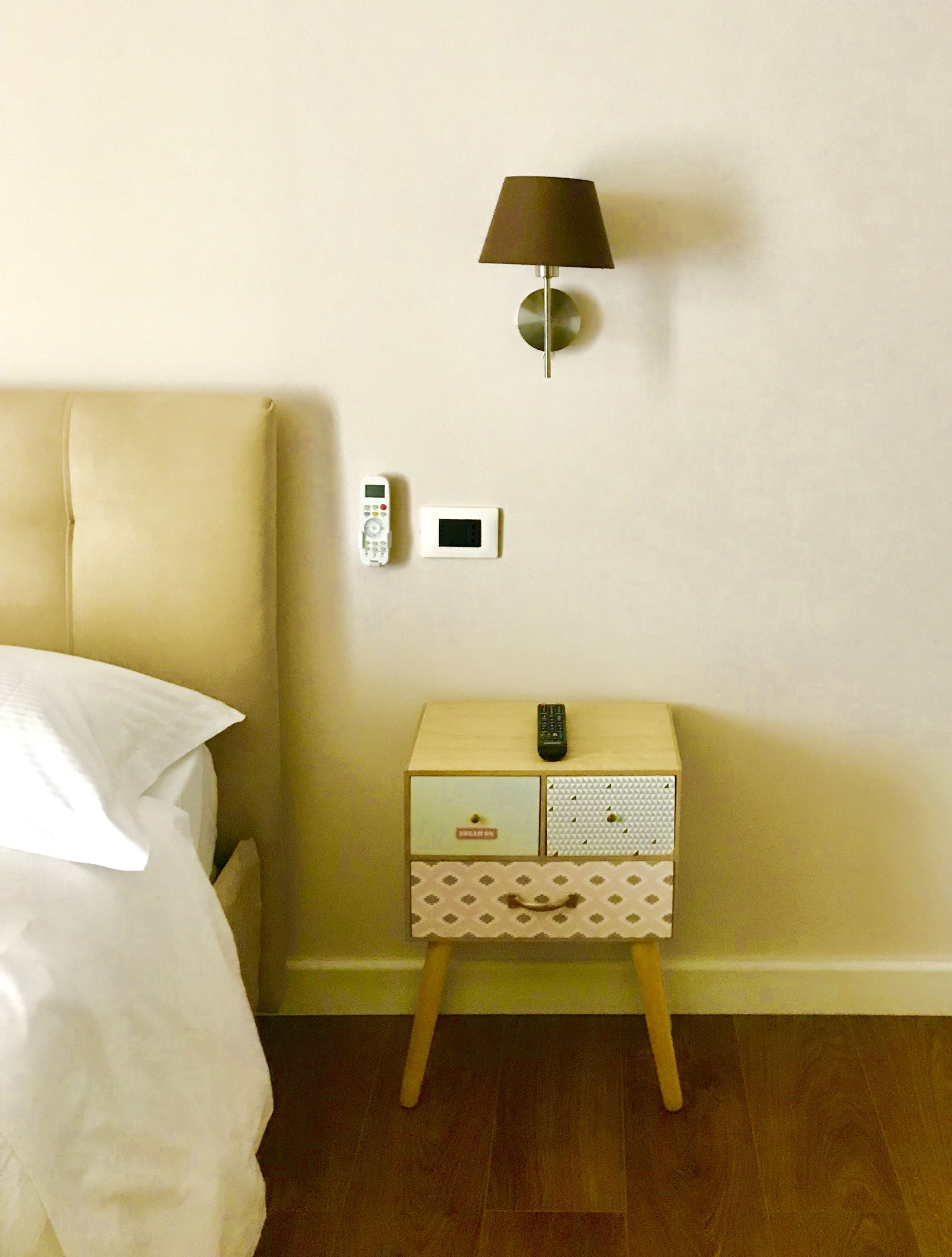 Un dormitorio con una cama, una mesita de noche con lámpara, un termostato y un control remoto.