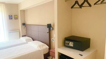 Habitación de hotel con dos camas, un escritorio pequeño con una radio, un calentador y un perchero.