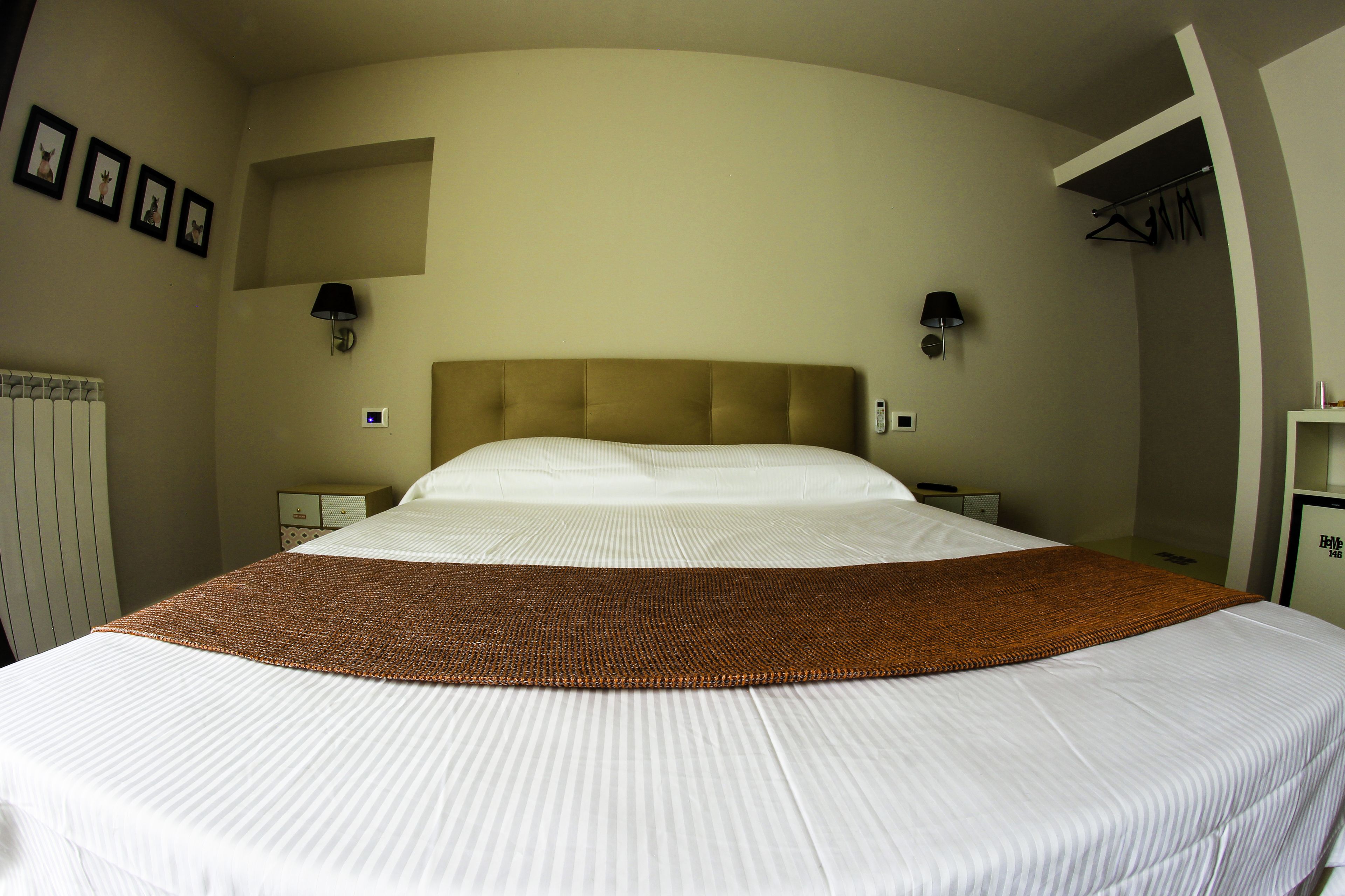 Ein ordentlich gemachtes Bett mit einer braunen Tagesdecke, zwei Nachttische mit Lampen und einem an der Wand befestigten Kleiderhaken.
