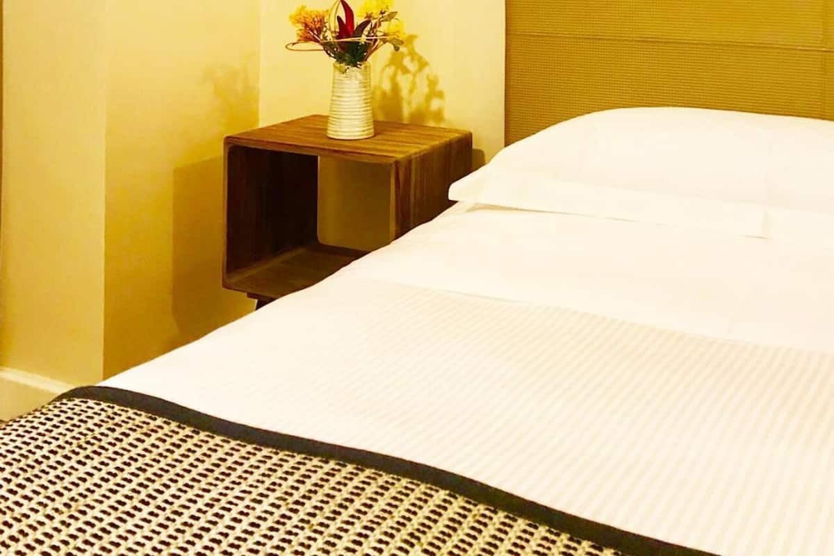 Ein Hotelzimmer mit einem Bett, einem Nachttisch mit Lampe und einer kleinen Vase mit Blumen.