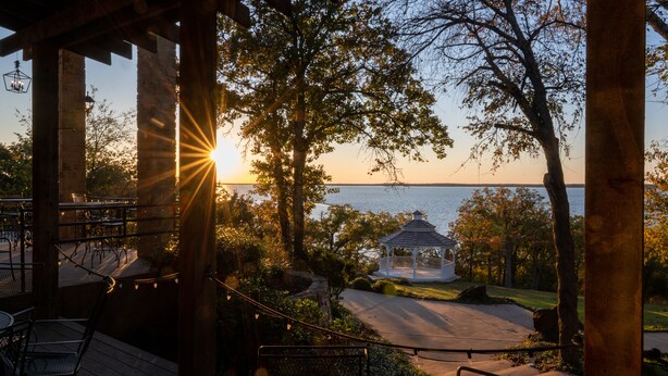 A gazebo with a view of the sunset over a body of water, surrounded by trees and outdoor seating.