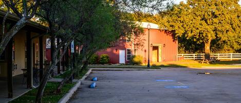 A parking lot with a red building, trees, and a white fence.