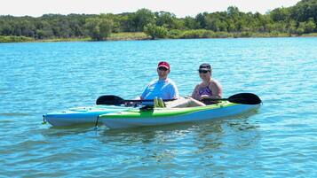 Deux personnes dans un kayak sur un lac paisible, avec une rive boisée en arrière-plan.