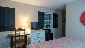 Un dormitorio con cama, escritorio, silla, cómoda, televisor y microondas.