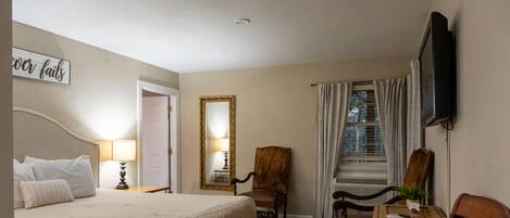 A hotel room with a bed, a desk, a chair, a television, and a mirror.