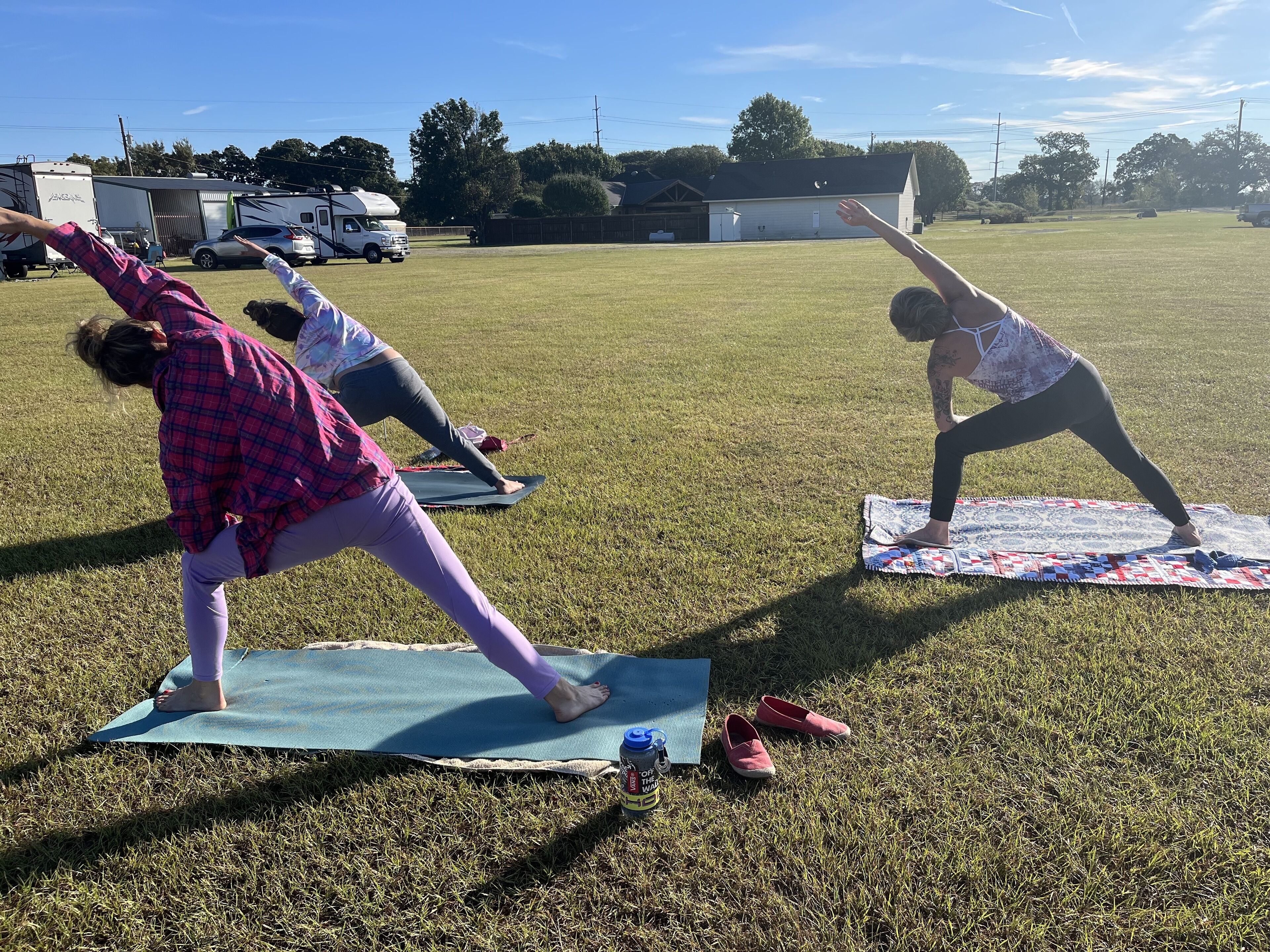 Three people practicing yoga on mats in an open grassy field.