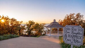A gazebo with a sign reading "THIS WAY TO Love, Laughter & Happily Ever After" near a body of water.