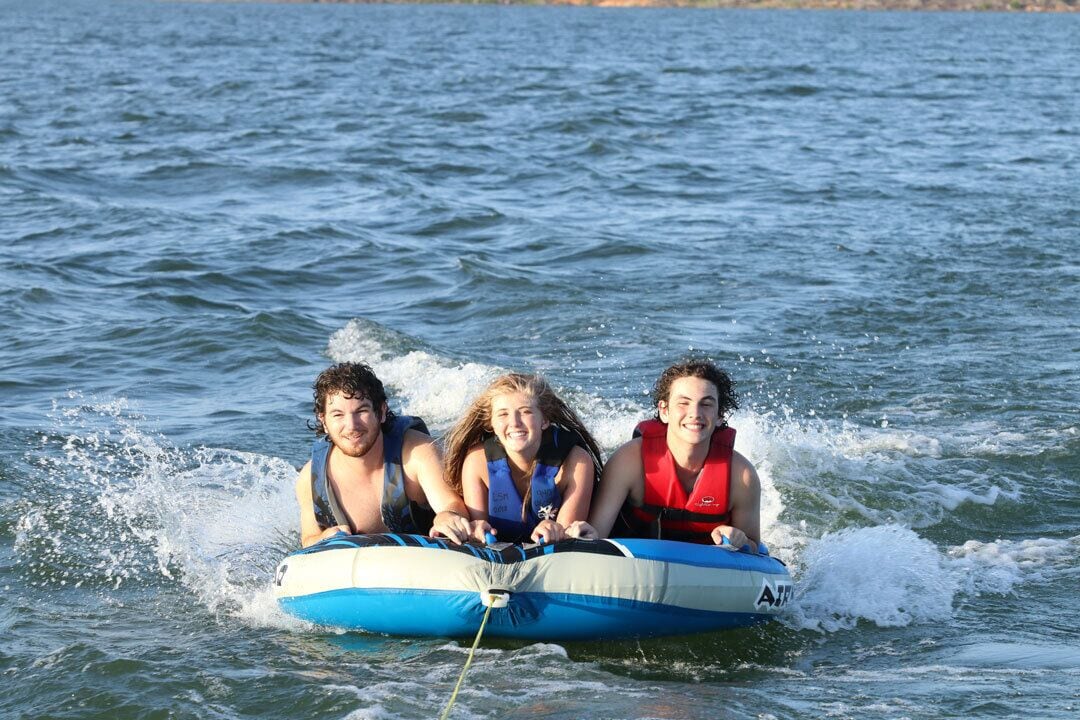 Three people on a blue and white inflatable raft in the water.