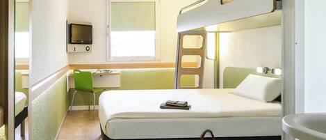 A compact hotel room with a bunk bed, a desk with a chair, a television, and a window.