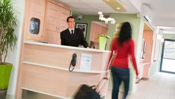 Un comptoir d’accueil d’hôtel avec un téléphone, un panneau indiquant si les chambres sont disponibles et une plante en pot.