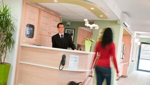 Een hotel receptiebalie met een telefoon, een bordje met kamervoorraad en een bloempot.