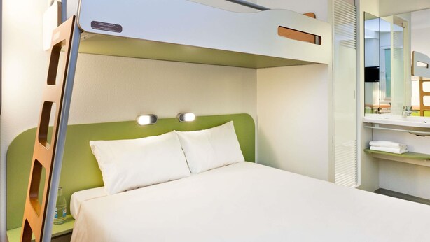 A bunk bed with a green headboard and two bedside lights, a small bedside table with a bottle, and a mirror above the bed. - Ibis Budget Augsburg Gersthofen (Gersthofen)