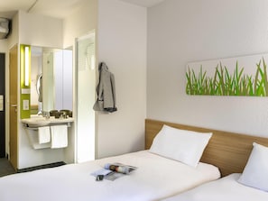 A hotel room with a bed, a bedside table, a mirror, a bathroom with a sink and towel rack.