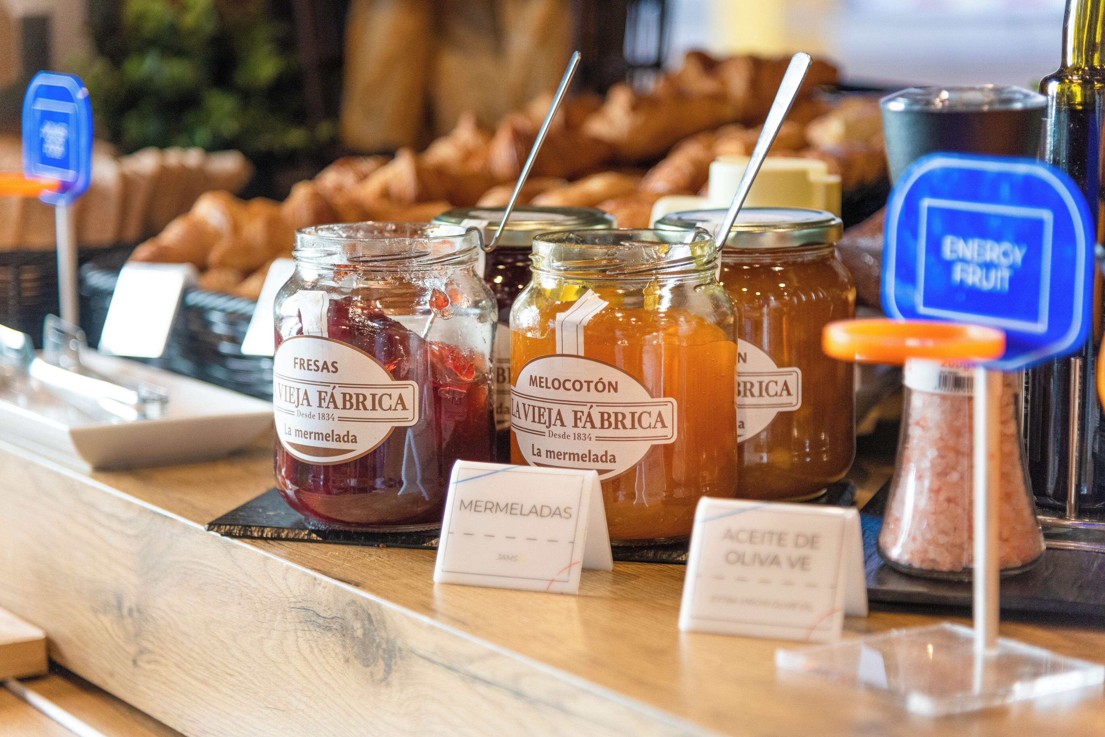 A display of jars labeled 'FRESAS VIEJA FÁBRICA' and 'MELLOCOTÓN VIEJA FÁBRICA' with labels 'La mermelada' and 'Aceite de oliva verde'.