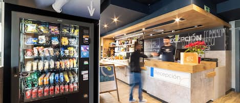 A modern reception area with a vending machine stocked with snacks and drinks, a wooden counter, and a chalkboard menu.
