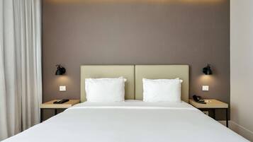 Une chambre d’hôtel avec un grand lit, deux tables de chevet et deux lampes fixées au mur.