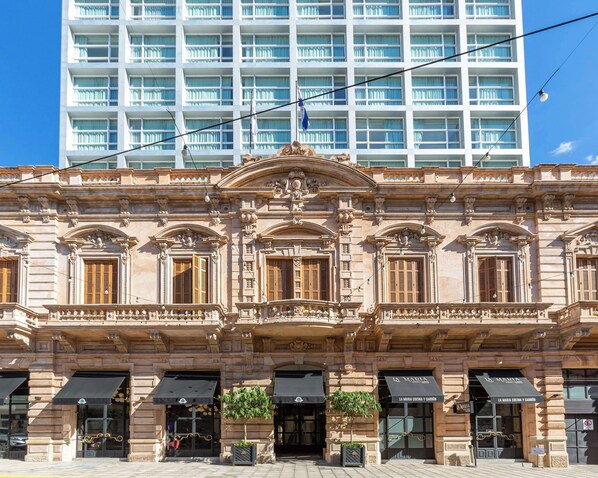 Un edificio histórico con arquitectura ornamentada, que presenta una entrada central con un arco decorativo y columnas, y un letrero que dice "La Maria Cocina y Carbón".