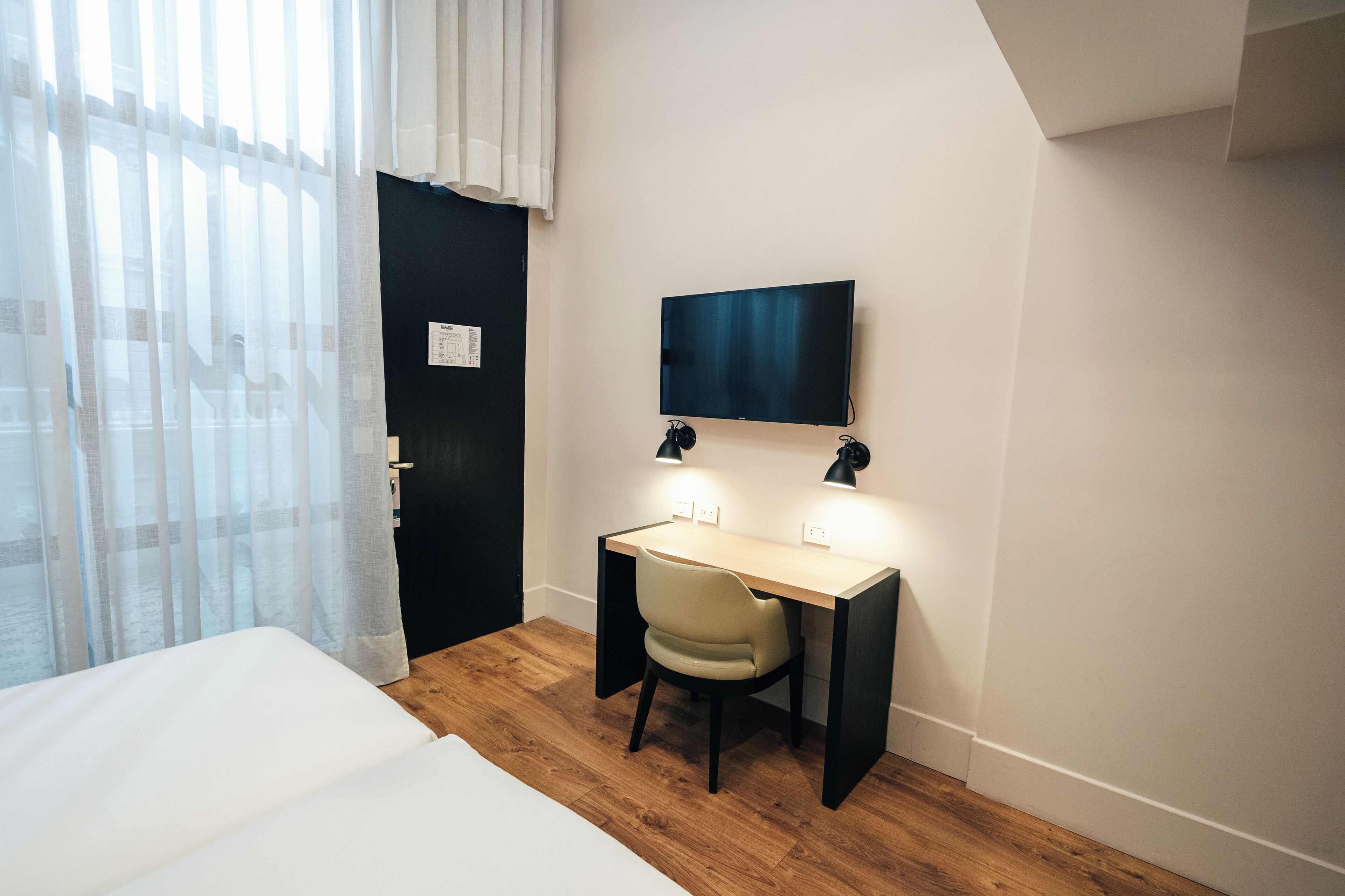 Une chambre à coucher avec un lit, un bureau, une chaise et un téléviseur fixé au mur.