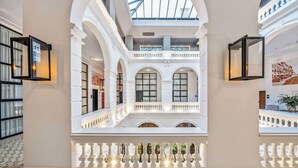 A spacious atrium with a high ceiling, large windows, and a central balcony with ornate railings.