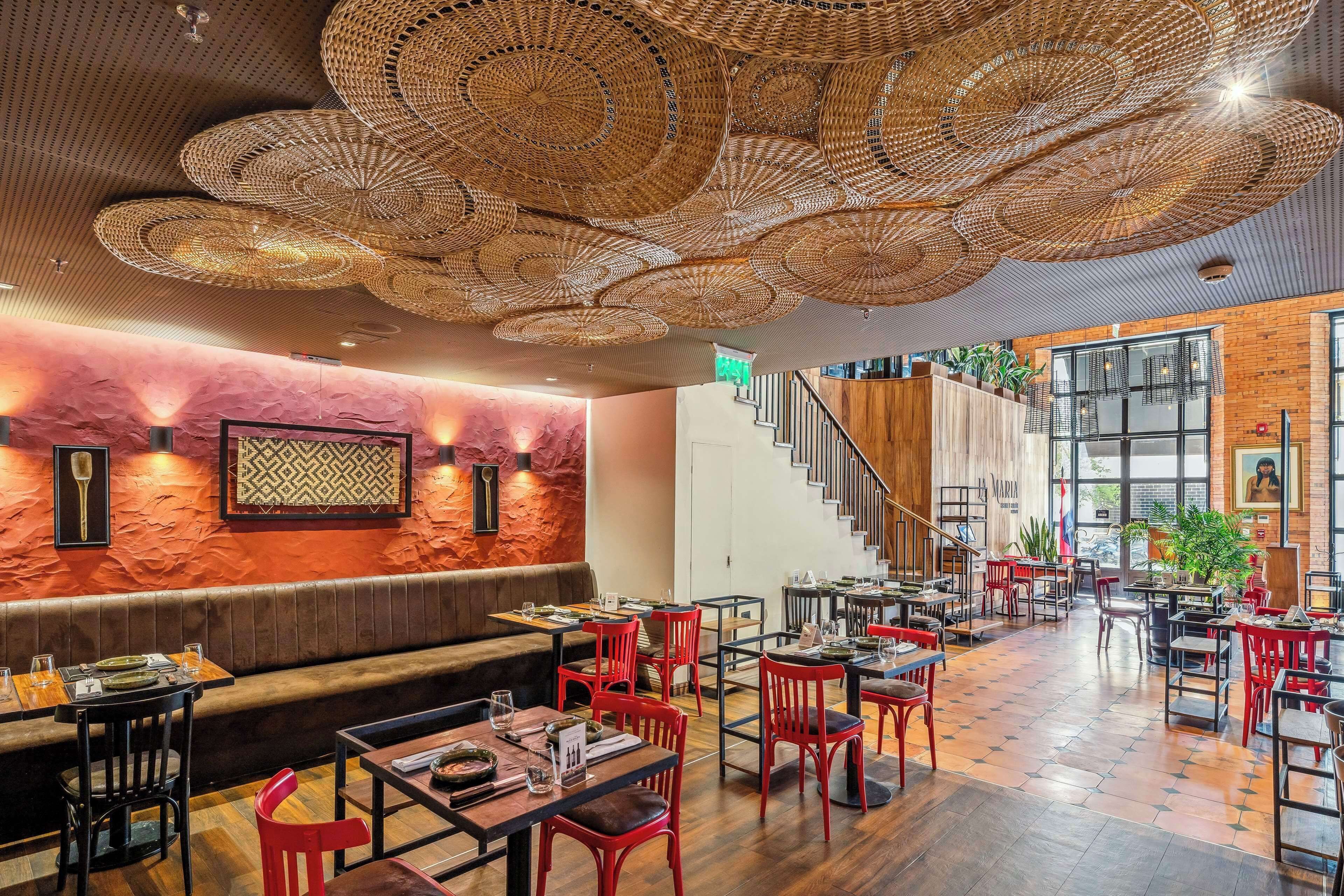 Un restaurante con una decoración moderna, que presenta un suelo de madera, sillas rojas y una escalera que conduce a un nivel superior.