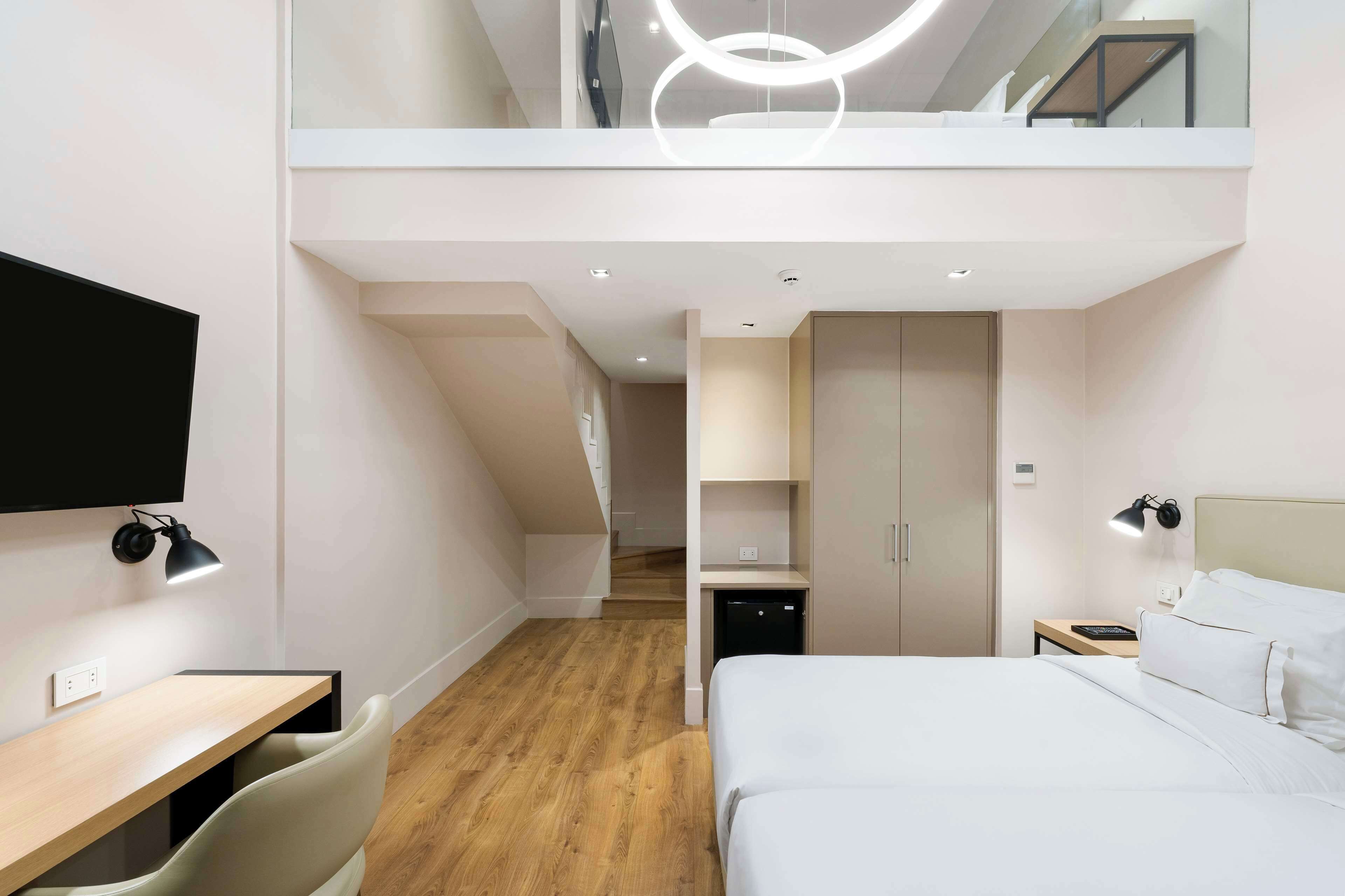 A modern hotel room with a desk, chair, bed, and a TV.