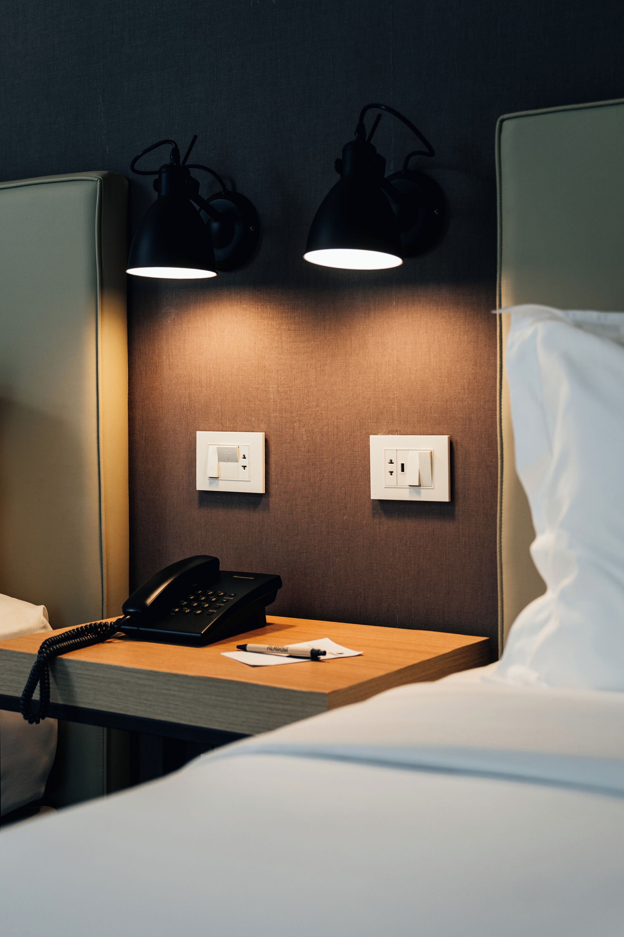 Habitació d'hotel amb una taula de nit, un telèfon, una làmpada i una presa de corrent.