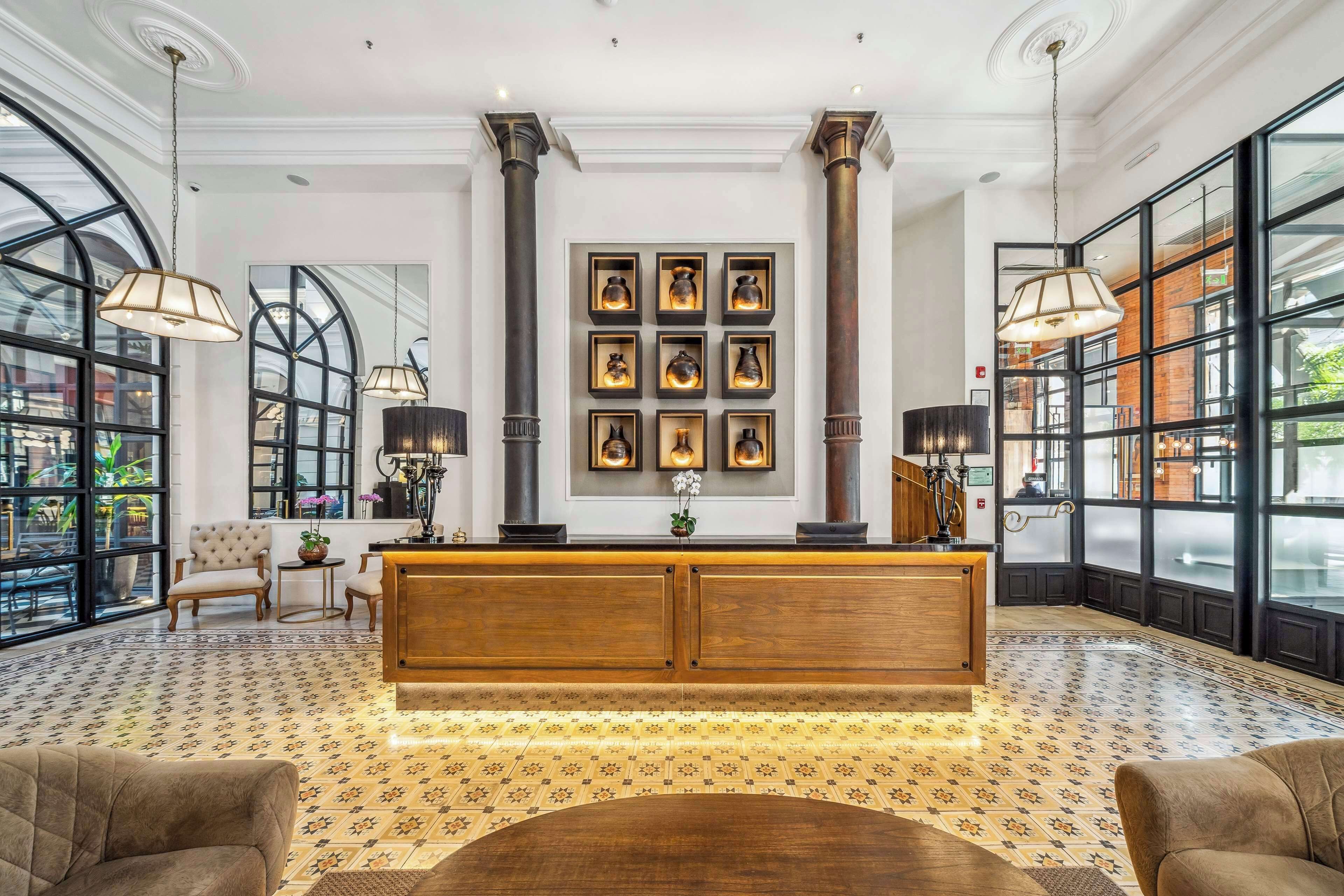 A lobby with a wooden reception desk, large windows, and a patterned floor.