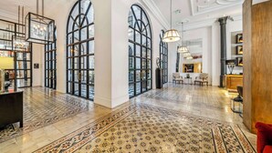 A spacious lobby with high ceilings, large arched windows, and patterned floor tiles.