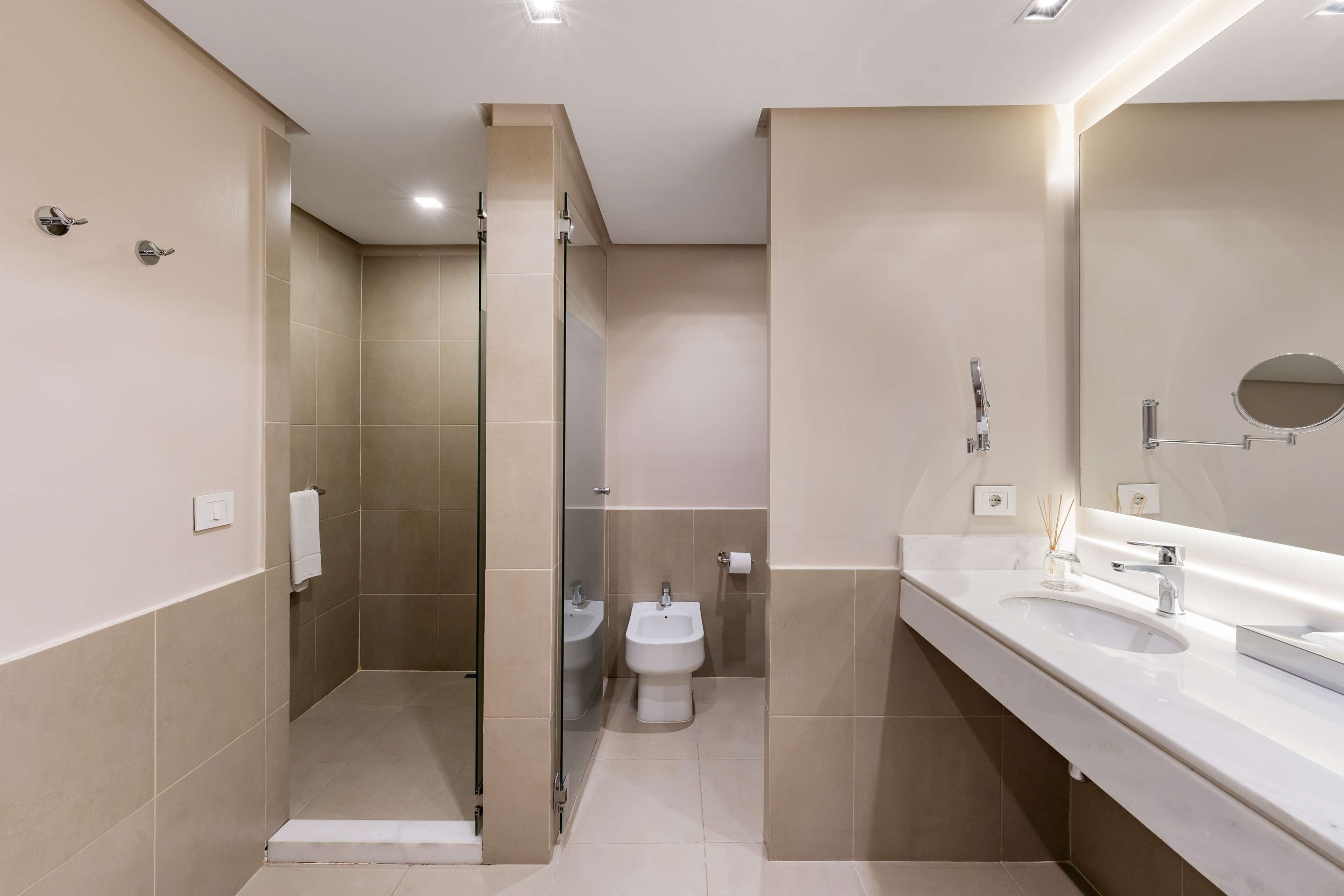 Un baño moderno con ducha a ras de suelo, un bidé y un mueble de tocador amplio con espejo.