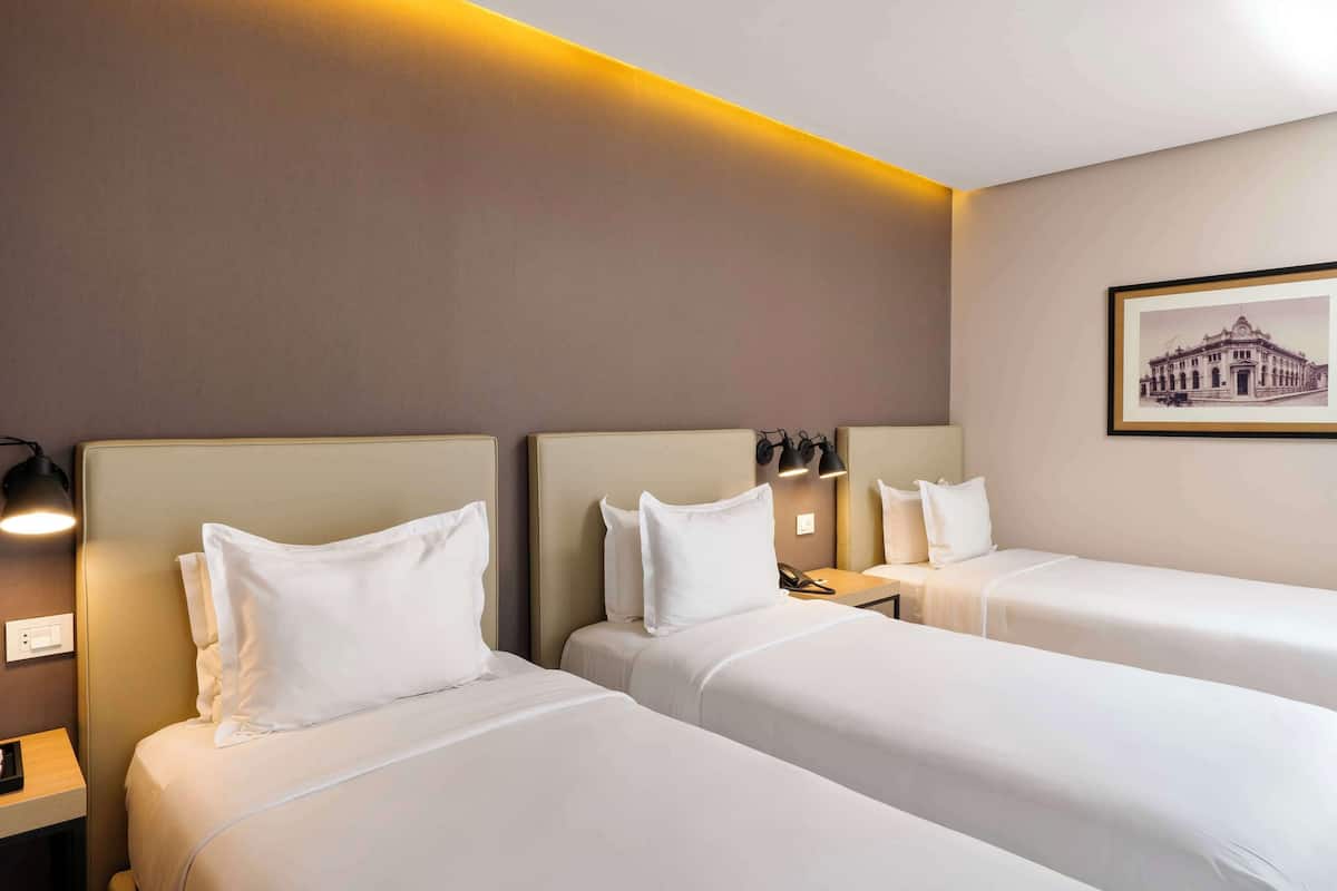 A hotel room with two single beds, a nightstand with a lamp, a framed picture on the wall, and a light strip above the beds.