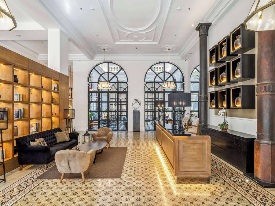 A spacious lobby with a black sofa, wooden bookshelves, a patterned floor, and a reception desk with framed items.