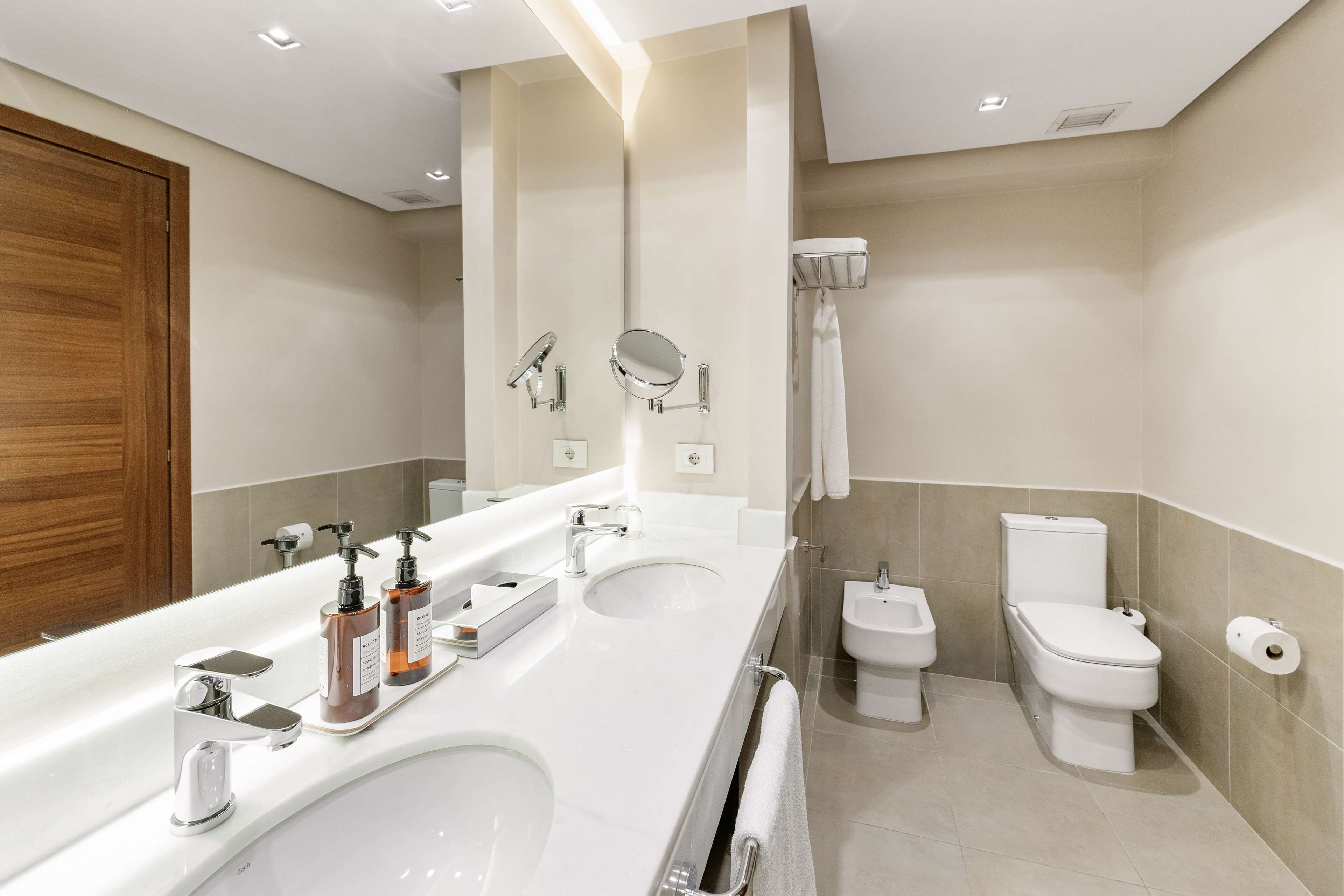 Une salle de bain moderne dotée d’un long meuble-lavabo, de deux vasques, de toilettes et d’un bidet.