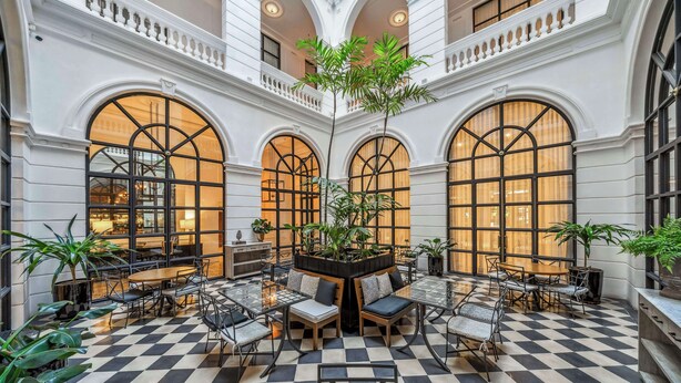 A spacious indoor area with checkered flooring, multiple seating arrangements, and large arched windows.
