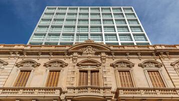 A building with a classical facade featuring ornate columns and detailed carvings, and a modern glass skyscraper above.