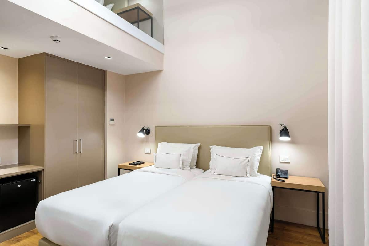 A modern hotel room with a large bed, bedside tables, a desk, and a wardrobe.