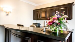 A kitchen with dark wooden cabinets, a curved countertop, a chair, a small table with a floral arrangement, and a wall-mounted light fixture. - The Hotel Hollywood (Los Angeles)