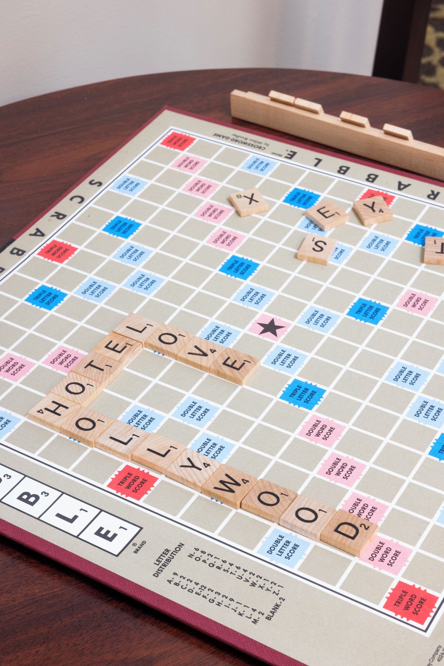 Un jeu de société Scrabble avec le mot « HÔTEL » épelé sur le plateau, des tuiles en bois représentant les lettres et une feuille de score.