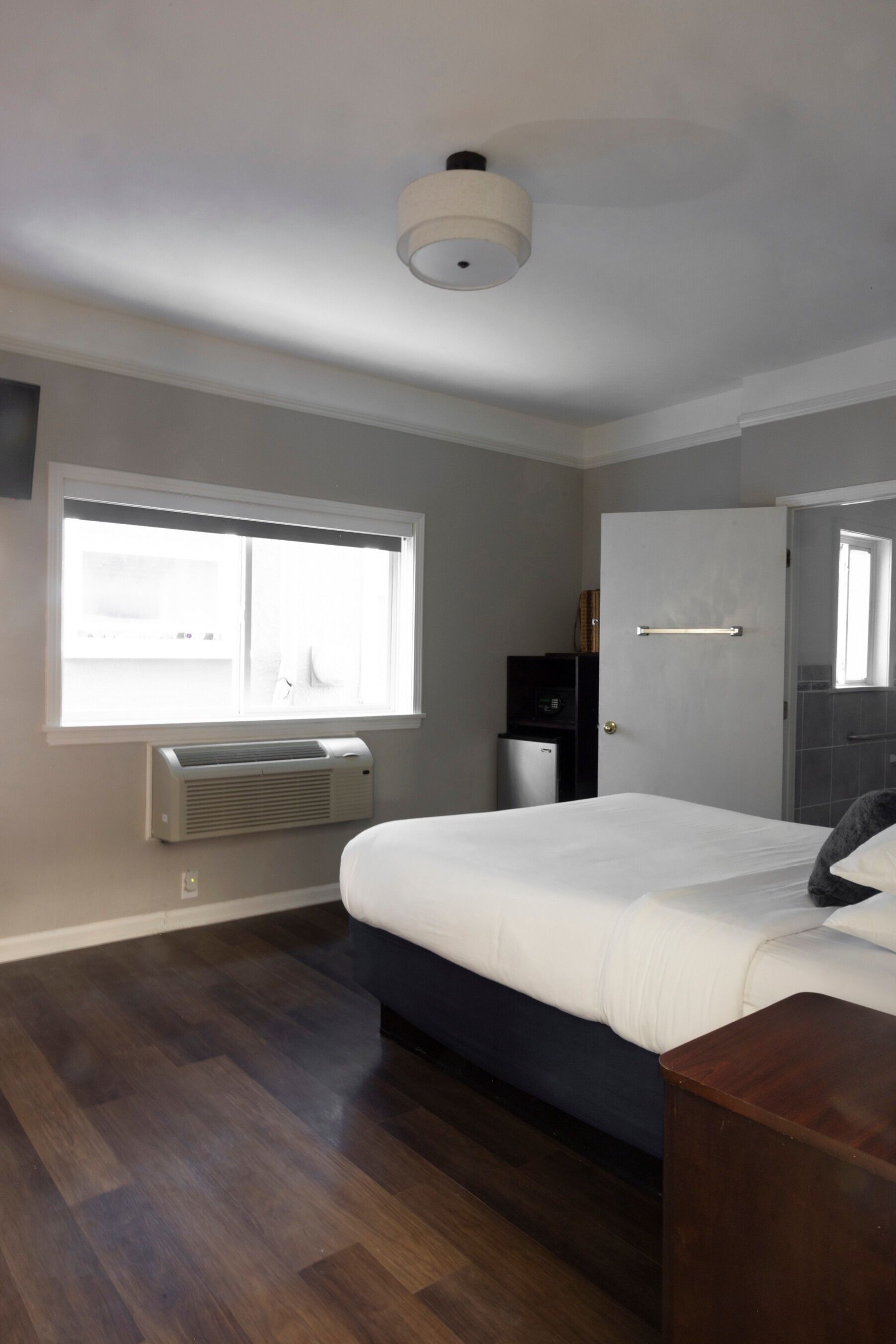 Une chambre à coucher comprenant un lit, une fenêtre, un appareil de climatisation, une porte et un petit bureau.