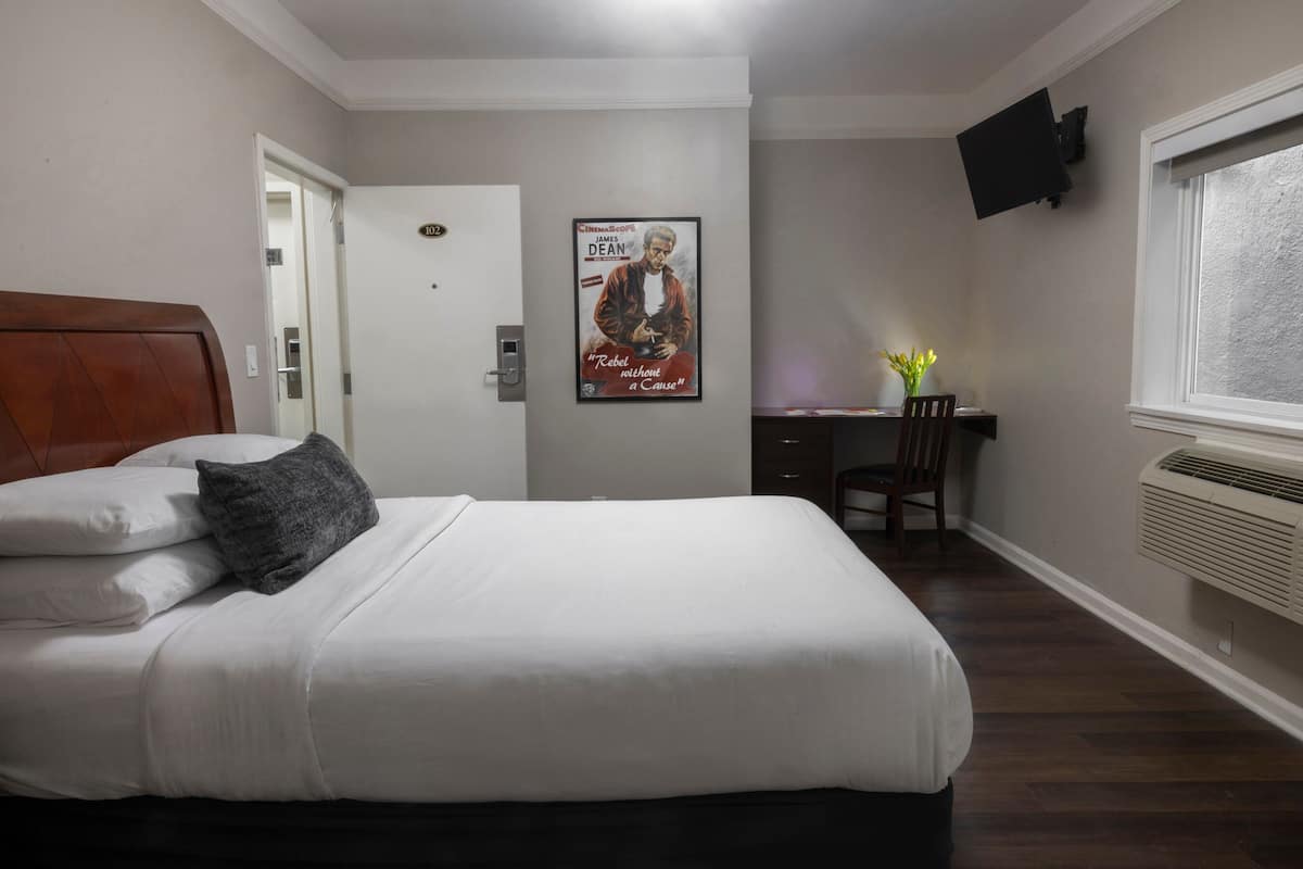 A bedroom with a bed, a desk, a chair, a poster, and a mounted TV.