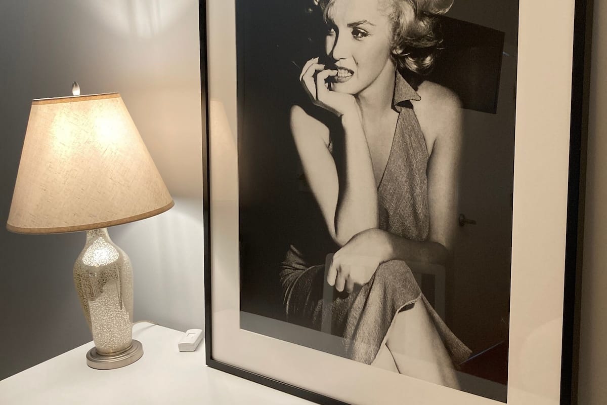 A framed black and white photograph on a white console table, next to a textured lamp.