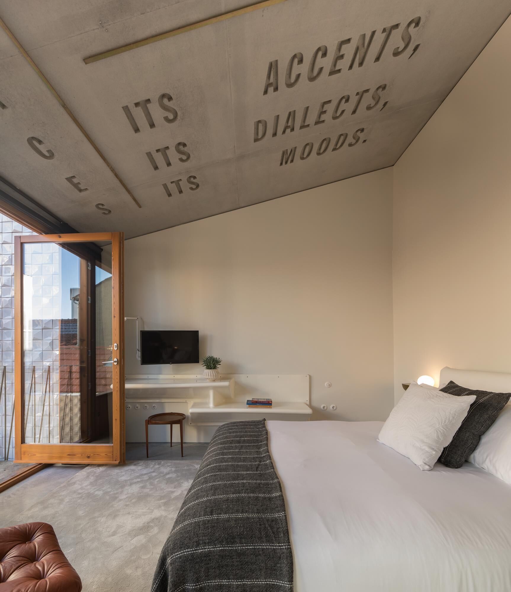 A bedroom with a bed, a desk, a TV, and a sliding glass door to a balcony.