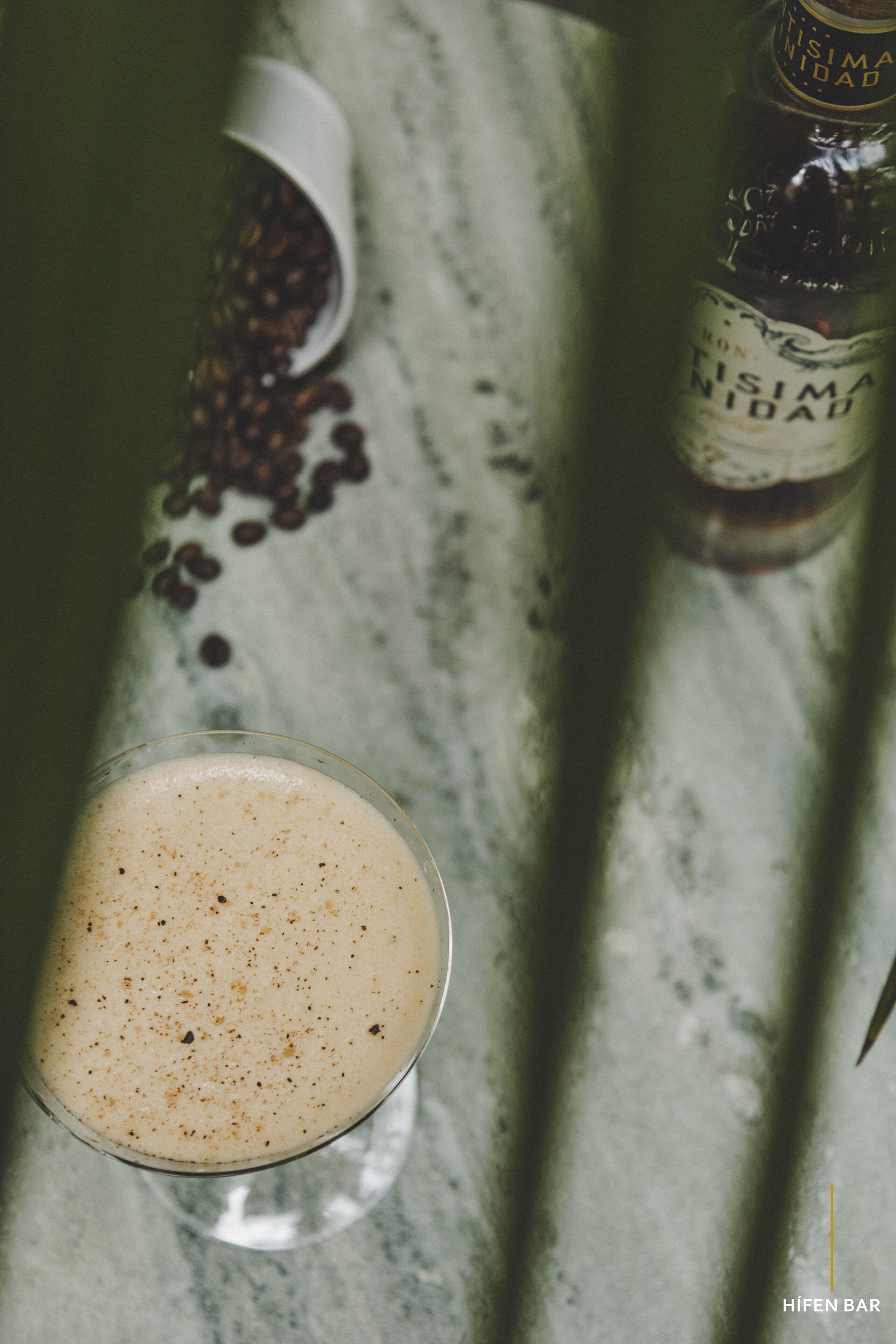 Un verre contenant une boisson, avec des grains de café dispersés sur une surface en marbre.