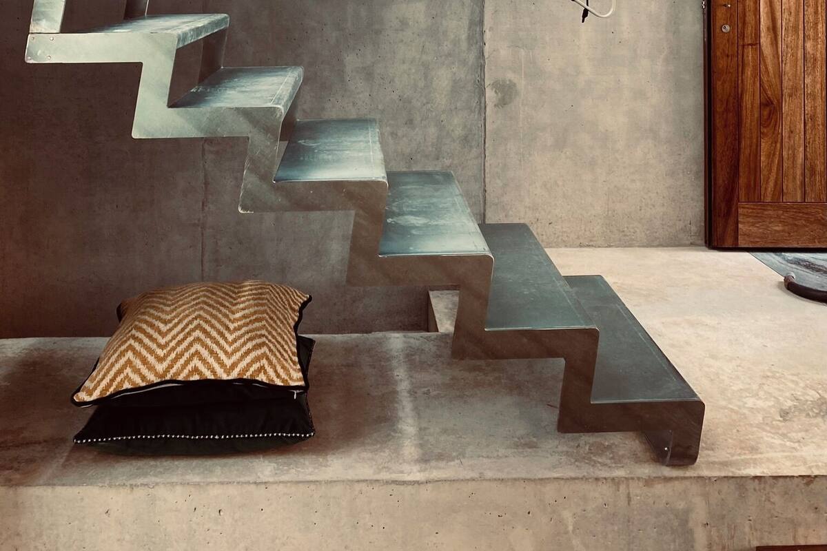 Una escalera moderna con barandilla metálica, una puerta de madera y un cojín estampado en el suelo.