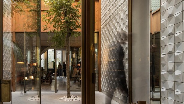Un edificio moderno con fachada de vidrio, un árbol en el patio y una persona caminando.