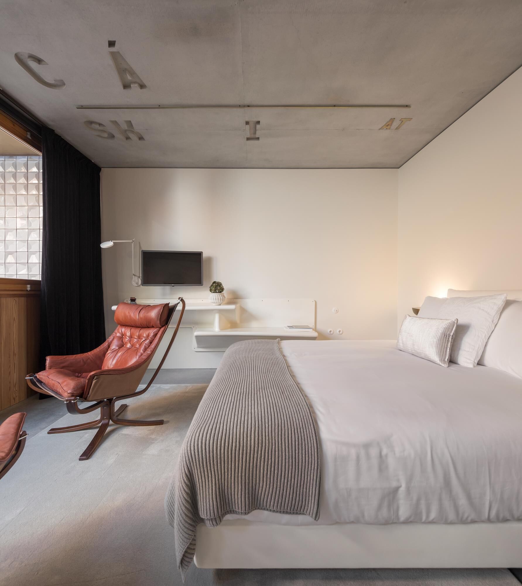 A modern hotel room with a large bed, a leather chair, a flat-screen TV, and a small table.