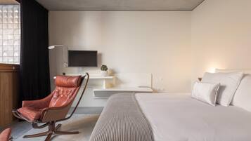 A modern hotel room with a large bed, a leather chair, a flat-screen TV, and a small table.