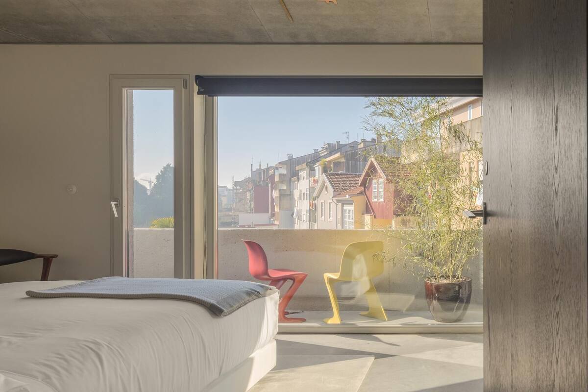 Un dormitorio con una cama, una silla roja, una silla amarilla y una planta en maceta.